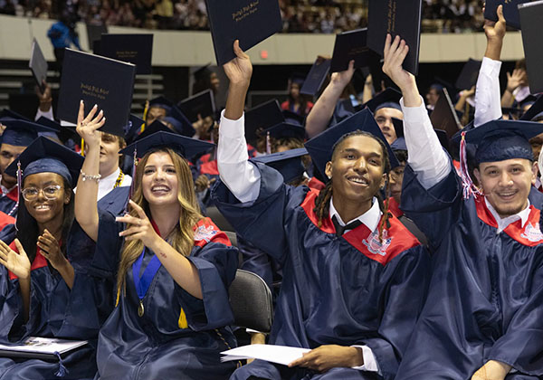 Graduates in caps and gowns celebrate, raising diplomas at a high school commencement ceremony.